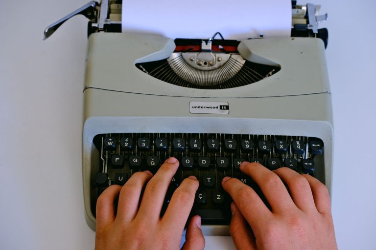 Hands typing on a grey manual typewriter with a sheet in the roller