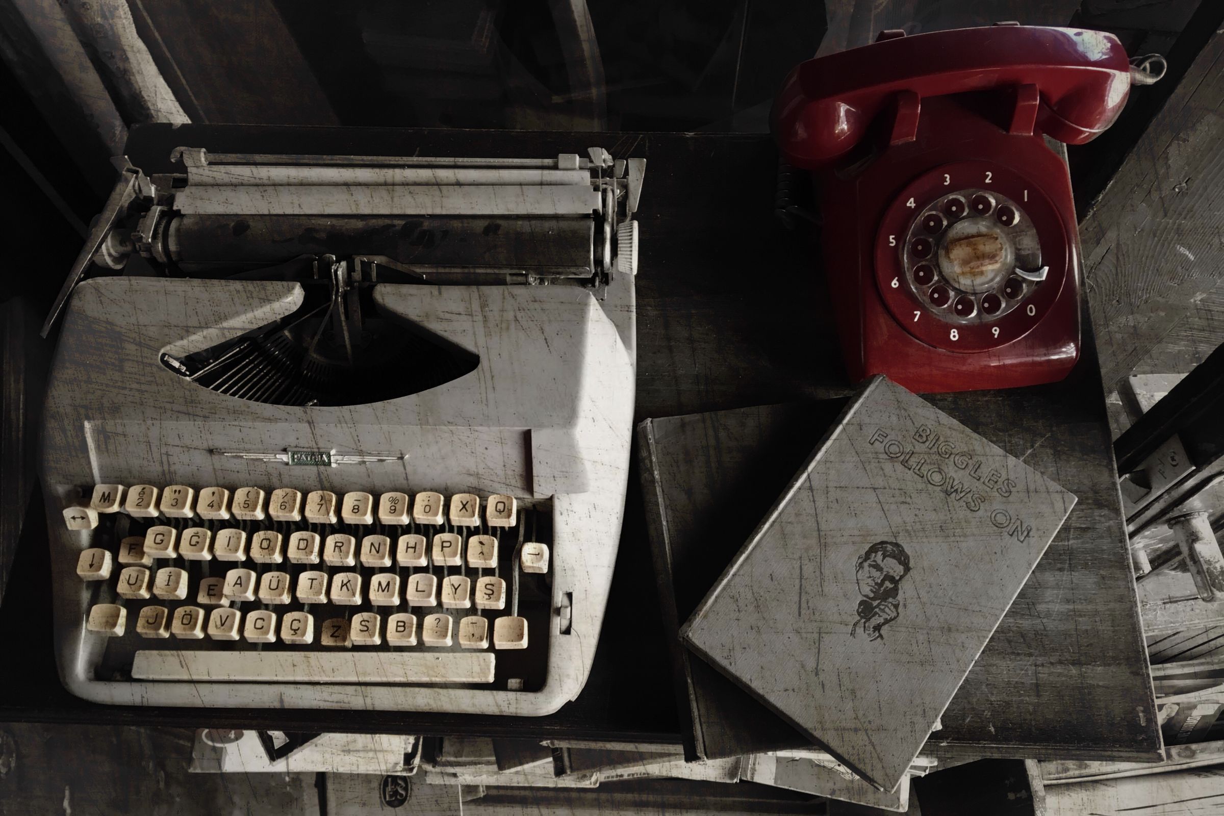 A manual typewriter beside a red rotary telephone on a desk